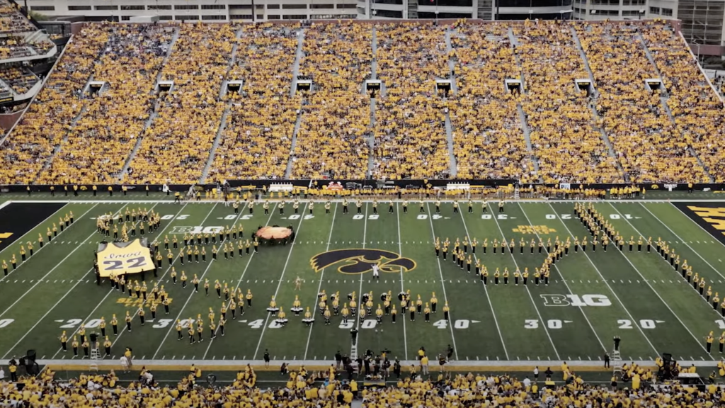HMB performing drill in Kinnick Stadium depicting Caitlin Clark shooting a "3" from the logo